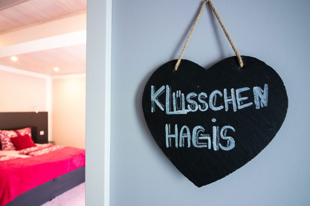 Selbstbemalte herzförmige Schieferplatte mit Schriftzug "Klüschen Hagis" hängt an einer Hotelzimmertür