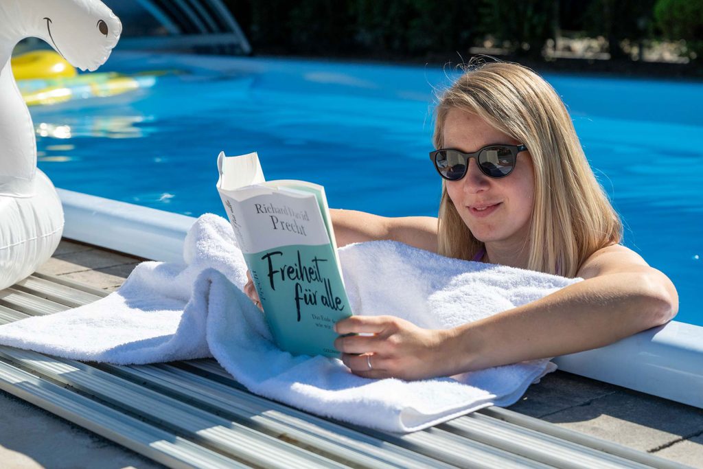 Frau ließt ein Buch am Beckenrand der Poollandschaft in der Pension zur Krone in Martinfeld